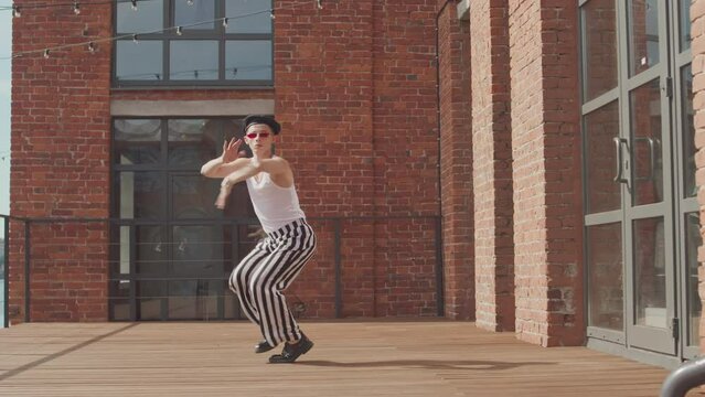 Full length slowmo of feminine boy in stylish vintage outfit voguing while walking towards camera outdoors
