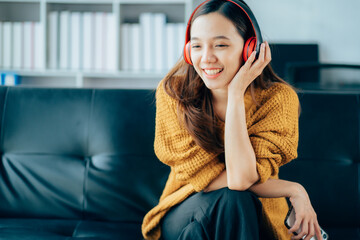 Beautiful young asian woman with headphones relaxing on the sofa. She is listening to music using...
