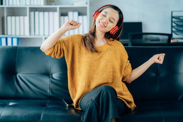 Beautiful young asian woman with headphones relaxing on the sofa. She is listening to music using...