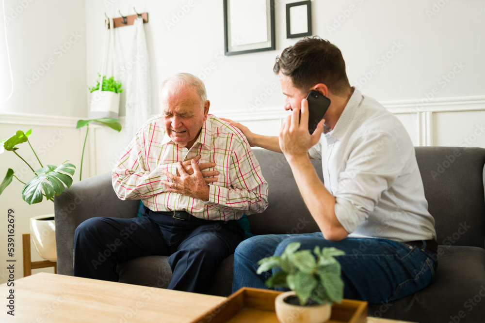 Wall mural Senior old man having a heart attack and getting help from his son