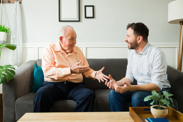 Cheerful elderly senior man and young man talking looking happy at home
