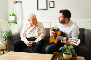 Cheerful son playing the guitar and enjoying music with his old father