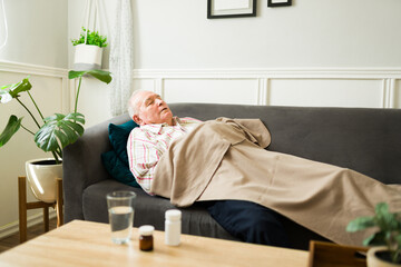 Sick elderly man taking medicine pills and sleeping on the sofa