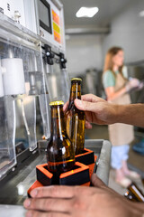 Close up of male brewer hands in a brewery filling bottles with beer.