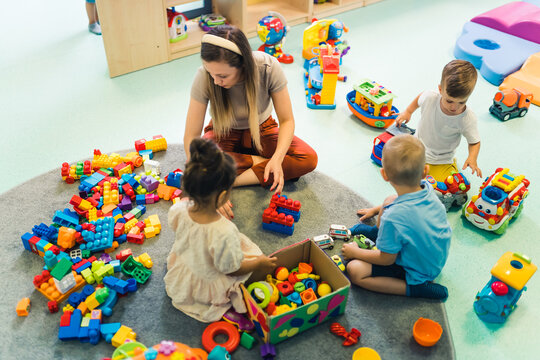 teacher and three preschoolers surrounded by the toys playing with building blocks at kindergarten, creative games for kids. High quality photo