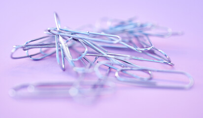 Paper clips together in pile, connected and a chain on purple background. Office supplies,...