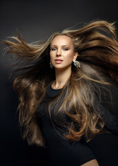 Close-up portrait of a young beautiful woman with gorgeous flying natural healthy shiny hair on a black background.  Beautiful high fashion model.  Fashionable salon hairstyle.
