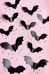 Minimal flat lay with black bats as halloween party vertical background. Pattern from paper decorations fly bats on pastel pink background for holiday card or invitation. Halloween concept