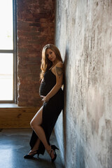 Fototapeta premium beautiful sexy pregnant brunette woman in black dress staying in studio and holding her belly