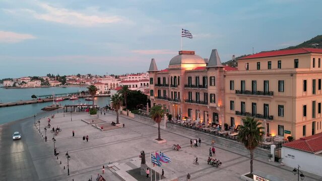 Flying orbit close around the Poseidonion Grand Hotel and main squar reavling the city and ocean of Spetses during sunset twilight
