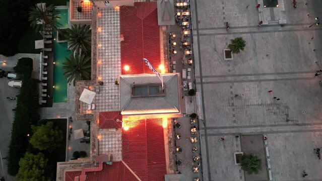 Flying over the Poseidonion Grand Hotel main squar showing the greek national glad on top of the roof revealing cityscape and lanscape of Spetses during twilight sunset