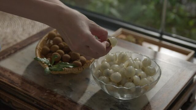 Peeling longan fruit in a bowl, sweet snack on a table