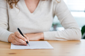 Close-up shot of an unidentifiable young woman filling out paperwork at her work desk