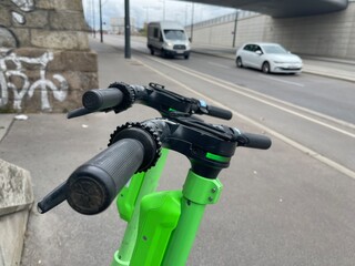 Close up cropped shot of handles of electric scooter parked in the city, cars on the road on background