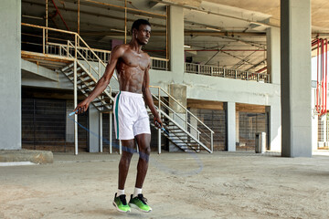 Muscular black man skipping rope. Portrait of muscular young man exercising with jumping rope concrete wall on background