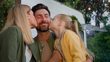 Caucasian happy loving family talking outdoors dad touching nose of little daughter child girl and mother wife kissing bearded father on cheek hugging love relationship affectionate cuddling together