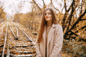beautiful long-haired woman walks through the autumn streets. Railway, autumn, woman in a coat.