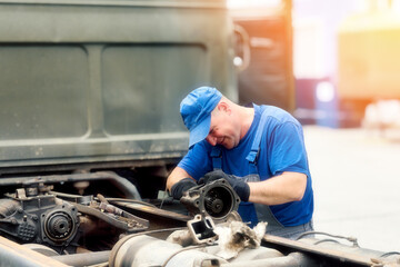 Mechanic in overalls repairs truck on summer day outside. Urgent repair of trucks. Authentic workflow..