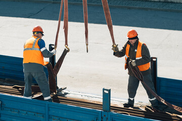Two slingers hook cargo to slings in back of truck. Real workers unload cargo. Slingers in...