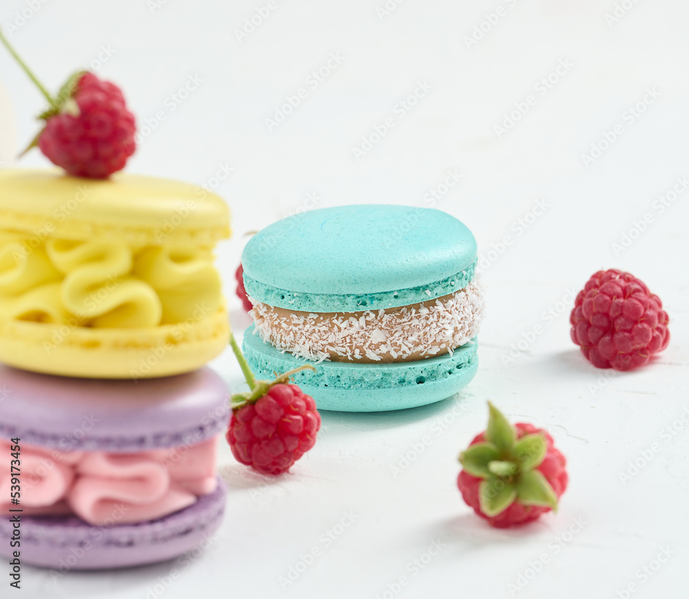 Poster stack of multicolored macaroons and red raspberries on a white background.
