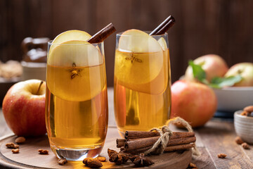Two glasses of apple cider with sliced apples and cinnamon