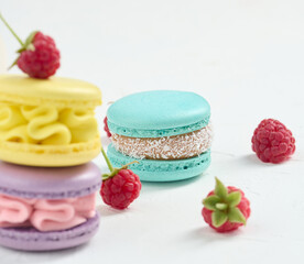 Stack of multicolored macaroons and red raspberries on a white background.