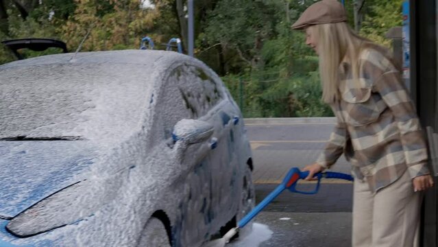 Woman washing a car in a self-service car wash station with wahing foam. Wash car self-service station