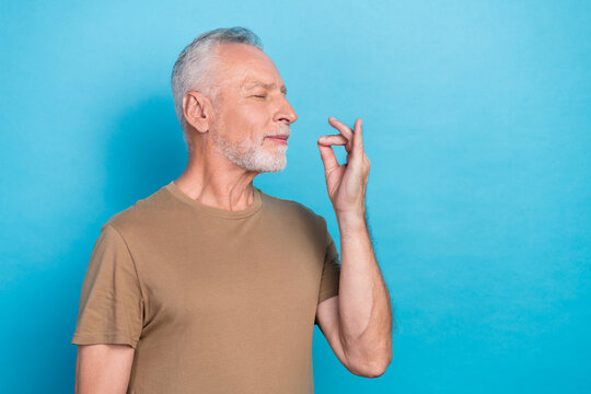 Portrait of satisfied retired man gray hair beard dressed beige t-shirt rejoice taste imaginary food isolated on blue color background