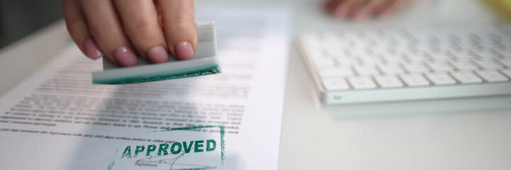 The hand puts the stamp approved on the document
