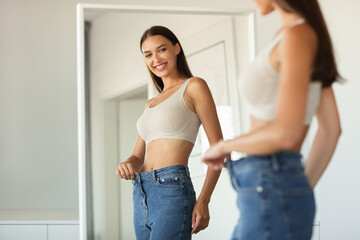 Lady Wearing Jeans After Slimming Comparing Size Near Mirror Indoors