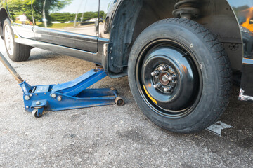 Hydraulic car jack lift car to replace punctured tyre with temporary emergency replacement tyre