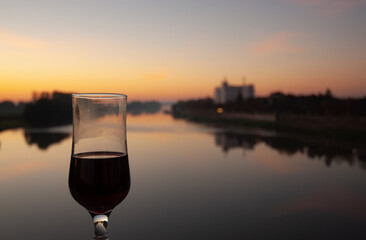 A glass of black wine on the bridge over the river in the sunrise.