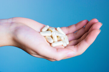 European woman hand on a blue background keeping many medicines white pills tablets antibiotics