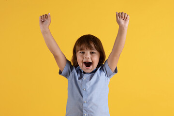 Emotional little boy shouting with raised hands, enjoying win, celebrating success, orange studio...