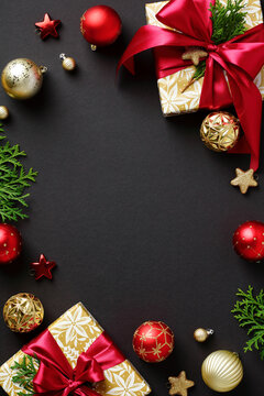 Christmas vertical banner. Frame made of gift boxes with red ribbon bow, fir branches, gold and red baubles on black background. Flat lay, top view, copy space.