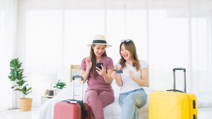 Two happy Asian women booked a hotel room on a smart phone and pay with a credit card while sitting...