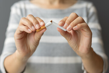 Close up young woman holding broken cigarette in hands. Happy female quitting refusing smoking...