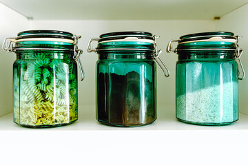 Glass green jars with sealed lid filled with bulk products stand in row on kitchen shelf.