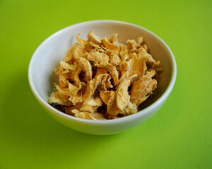 pieces of dried ginger lie in a white plate on a green background.  side view.  cooking spices