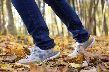Female legs in jeans and sneakers on fallen maple leaves. Girl running in autumn park