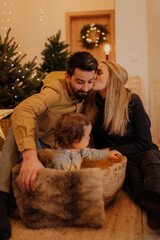 The little girl sitting in the basket plays with the lights in front of the fireplace and the parents enjoy watching