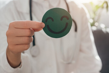 Close up of professional doctor female in coat and stethoscope holding small green happy smiley,...