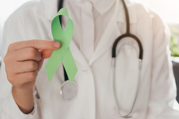 Close up of woman doctor in white coat with stethoscope holding lime green ribbon sitting on couch, Mental health awareness, world mental health day, world kidney day, organ donation concept - Powered by Adobe