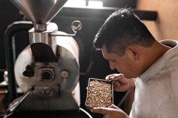 An Hispanic man is smelling the roast of the beans from the coffee roaster machine