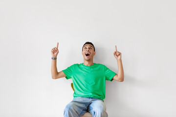 Excited arab man pointing and looking up at copy space, opening mouth in shock on light studio wall background