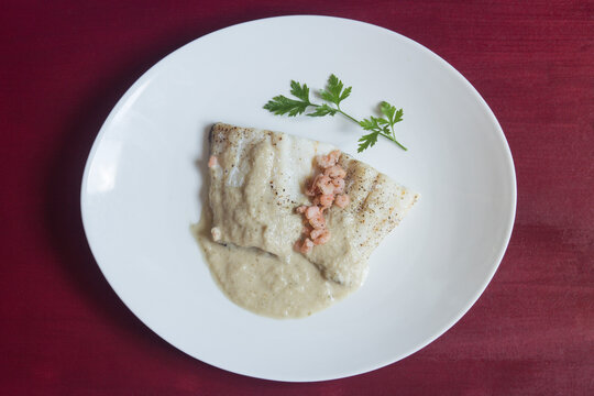 Overhead View Of A Presentation Food Plate Of Cod With Green Sauce On An Elegant Plate Garnished With A Sprig Of Fresh Parsley On A Table With Red Painted Wood Texture. Healthy White Fish Recipe.