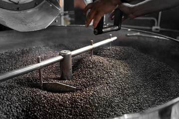 An Hispanic man is using a lever to release the coffee beans from the roaster machine
