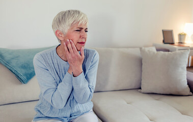 Photo of depressed ill mature woman having toothache and touching cheek. Mature woman suffering from tooth pain, caries. Gray hair female suffering from toothache, closeup.