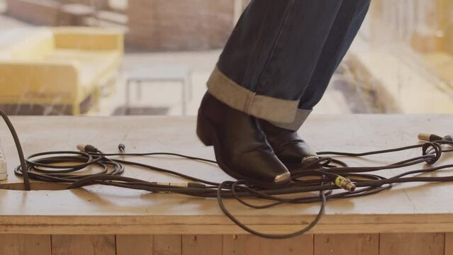 Low section of unrecognizable dancer in vintage blue jeans and pointed shoes voguing on wooden floor and tangling in long black cords