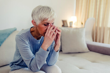 Photo of Woman suffering from stress or a headache grimacing in pain as she holds forehead with her hand, with copy space. Caucasian middle age woman looking sad.